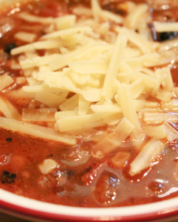 A bowl of easy frugal taco soup in a white bowl with cheddar cheese on top.