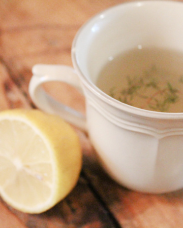 A tea cup of honey lemon tea for sore throats sitting on a countertop next to half a lemon.